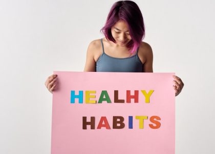 Asian woman holding a colorful 'Healthy Habits' sign in a studio setting, promoting wellness.